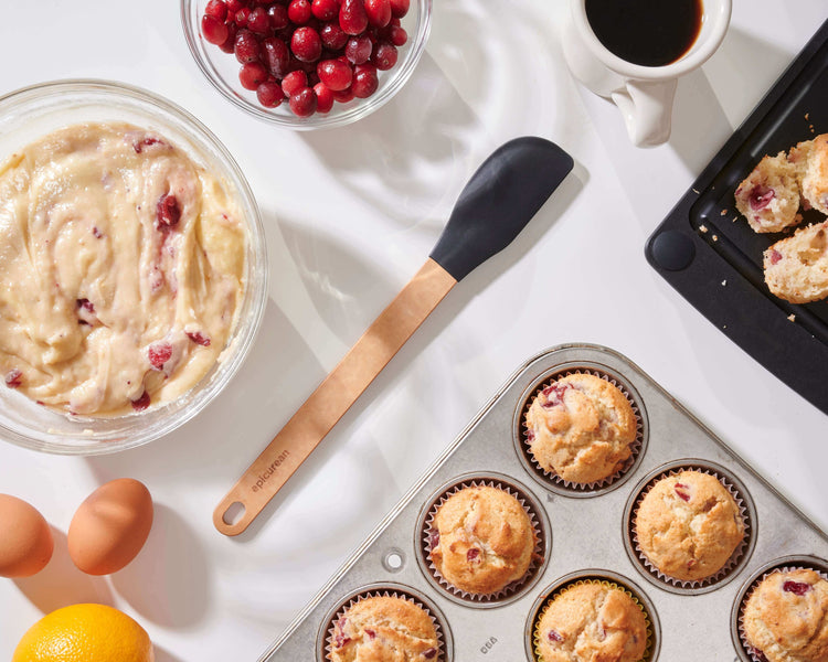 Silicone Series Natural/Black Small Spatula on a white counter with all of the ingredients to bake cranberry muffins and enjoy a cup of coffee